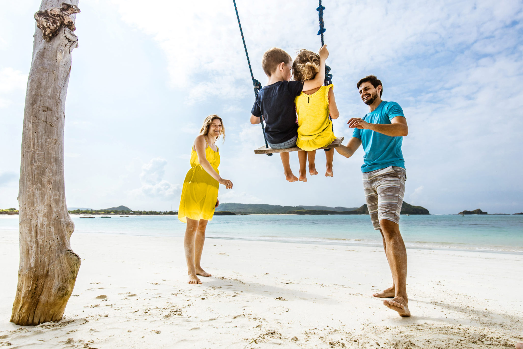 young parents swing their small kids during a summer day on the beach